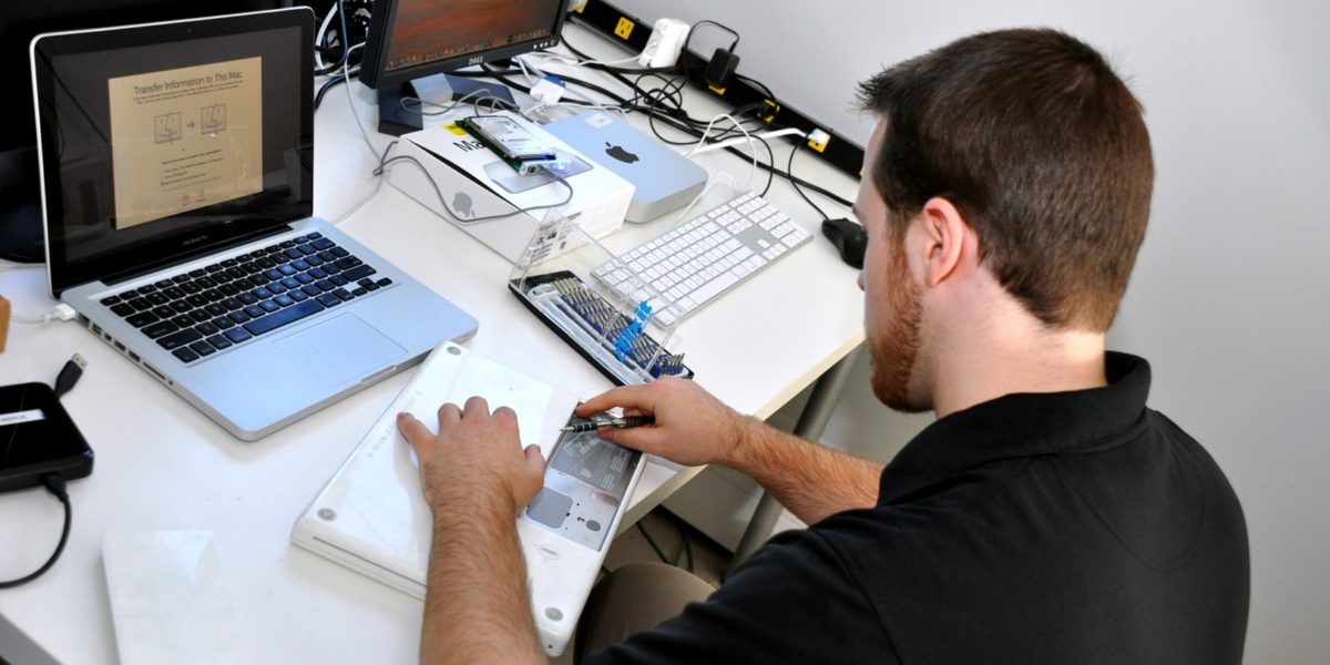 A man working on an electronic device at a cluttered desk with various tools and gadgets.